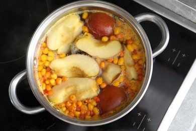Photo of Making compot of apples and sea buckthorn berries. Simmering fruits in pot on stove, top view