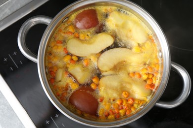 Photo of Making compot of apples and sea buckthorn berries. Simmering fruits in pot on stove, top view