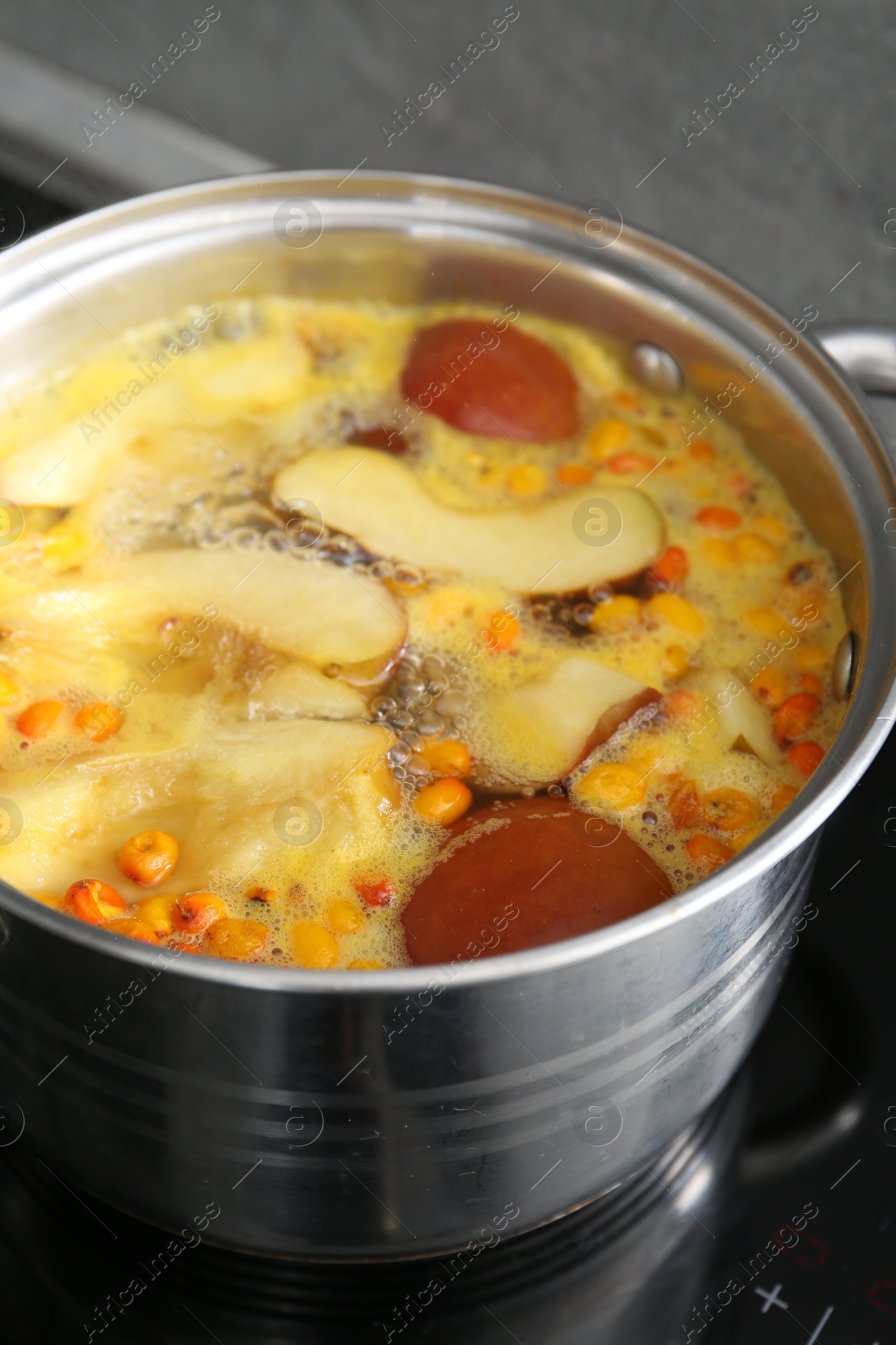 Making compot of apples and sea buckthorn berries. Simmering fruits in pot on stove, closeup Photo of Making compot of apples and sea buckthorn berries. Simmering fruits in pot on stove, closeup