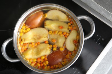Photo of Making compot of apples and sea buckthorn berries. Simmering fruits in pot on stove, top view