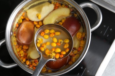 Photo of Taking tasty compot with ladle from pot on stove, top view