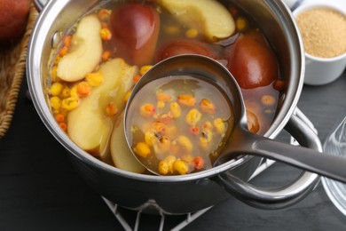 Photo of Taking tasty compot with ladle from pot on grey wooden table, closeup
