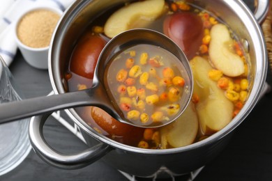 Photo of Taking tasty compot with ladle from pot on grey wooden table, closeup