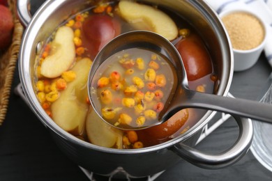 Photo of Taking tasty compot with ladle from pot on grey wooden table, closeup