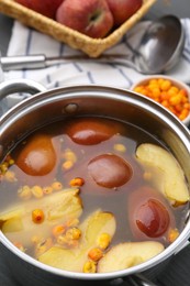 Photo of Tasty compot of apples and sea buckthorn berries in pot on grey wooden table, closeup