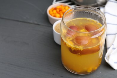 Photo of Tasty compot in glass jar and ingredients on grey wooden table, closeup. Space for text