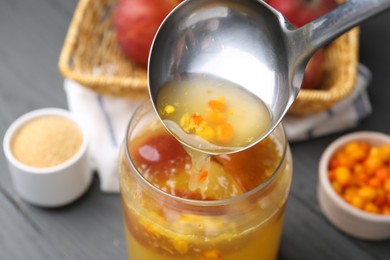Photo of Pouring tasty compot into glass jar on grey wooden table, closeup