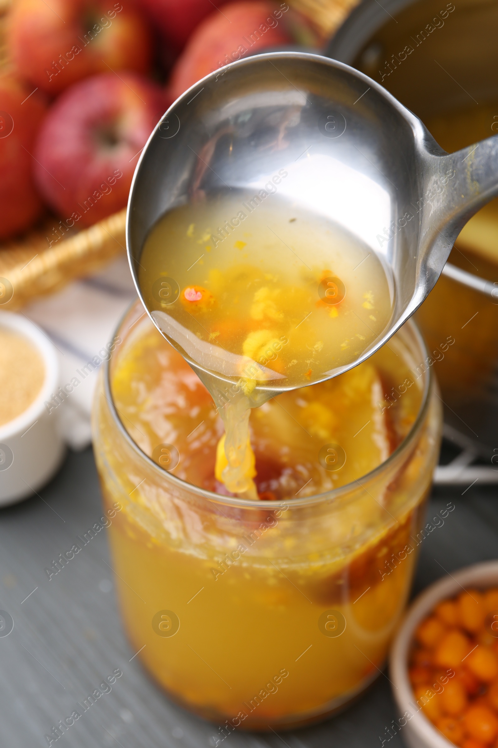 Photo of Pouring tasty compot into glass jar on grey wooden table, closeup