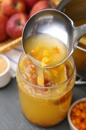 Photo of Pouring tasty compot into glass jar on grey wooden table, closeup