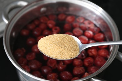 Photo of Adding sugar into tasty cherry compot in pot on stove, closeup