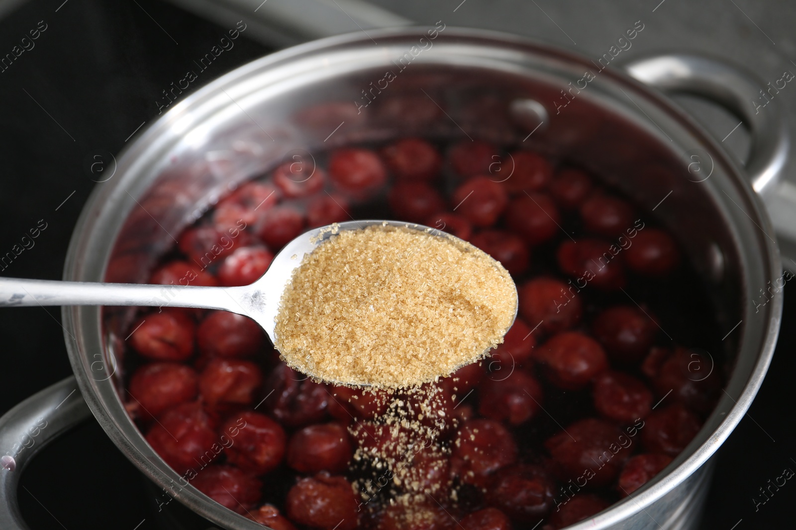 Photo of Adding sugar into tasty cherry compot in pot on stove, closeup