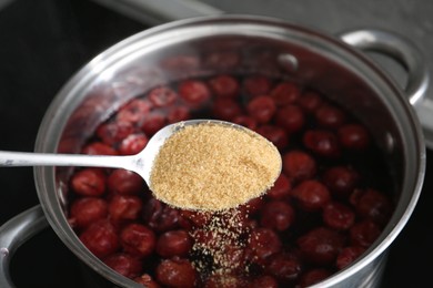 Photo of Adding sugar into tasty cherry compot in pot on stove, closeup