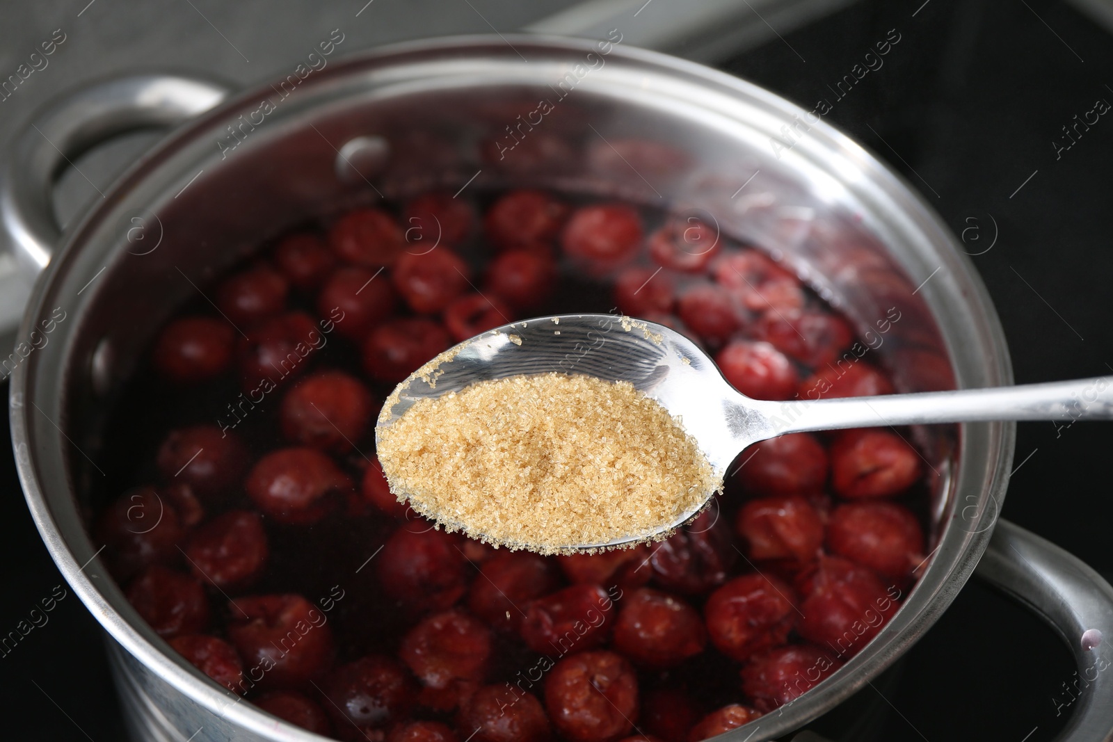 Adding sugar into tasty cherry compot in pot on stove, closeup Photo of Adding sugar into tasty cherry compot in pot on stove, closeup