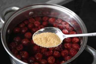 Photo of Adding sugar into tasty cherry compot in pot on stove, closeup