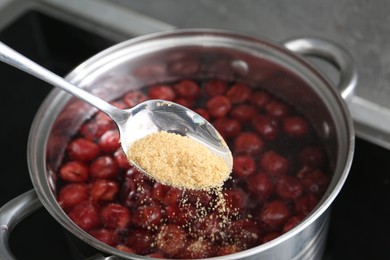 Photo of Adding sugar into tasty cherry compot in pot on stove, closeup