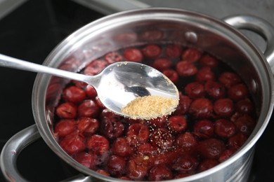 Photo of Adding sugar into tasty cherry compot in pot on stove, closeup