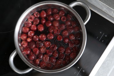 Photo of Making compot of cherries. Simmering fruits in pot on stove, top view