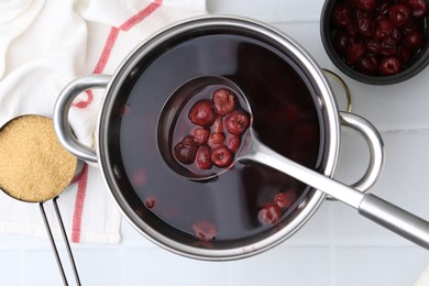 Photo of Tasty cherry compot in pot on white tiled table, flat lay
