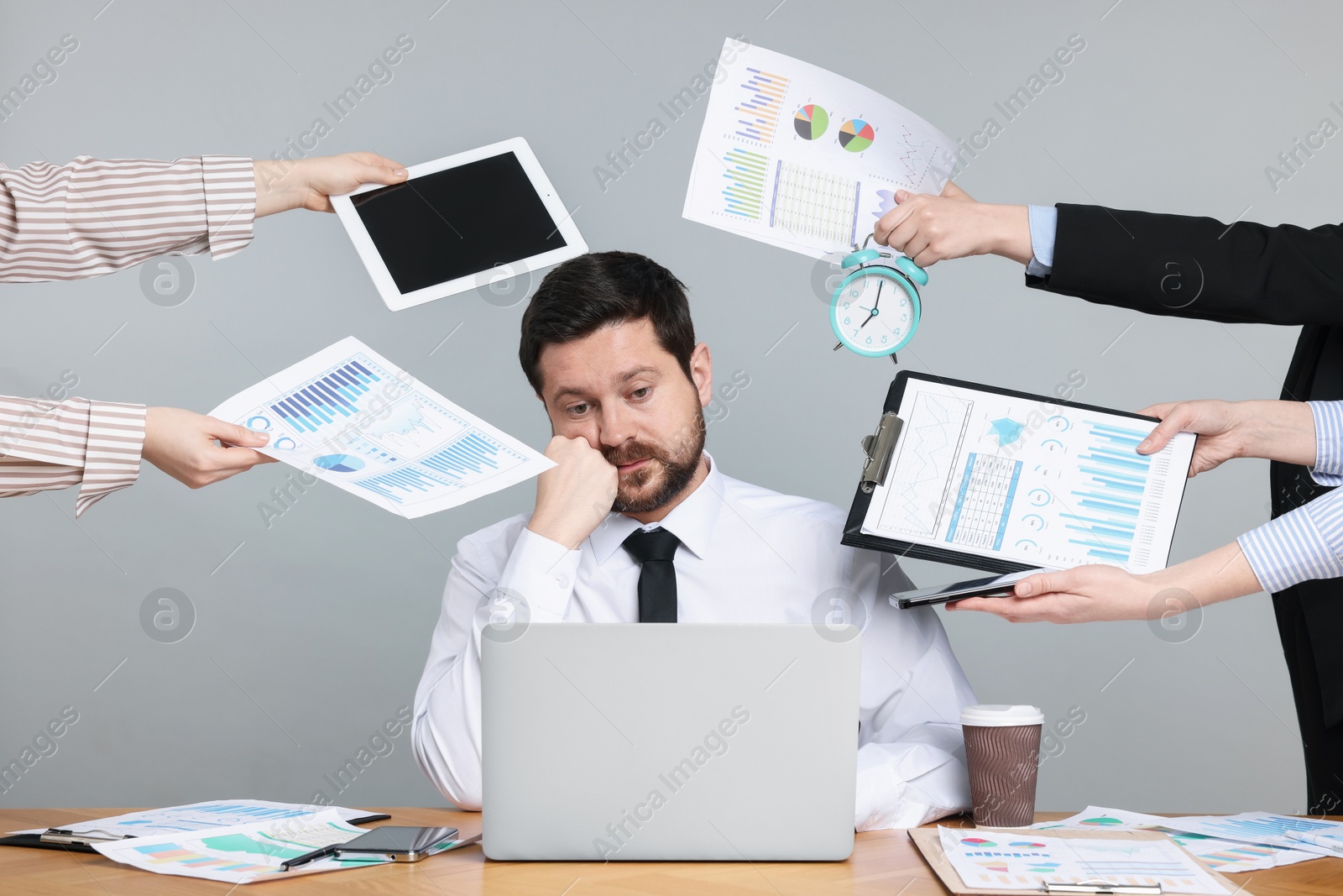 Man overwhelmed by different requests from colleagues at desk on light grey background Photo of Man overwhelmed by different requests from colleagues at desk on light grey background