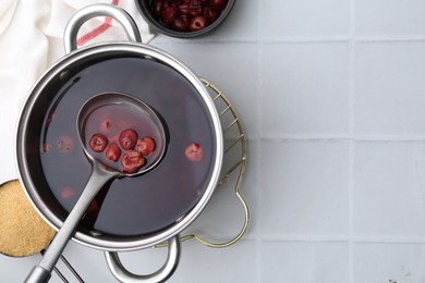 Photo of Tasty cherry compot in pot on white tiled table, flat lay. Space for text