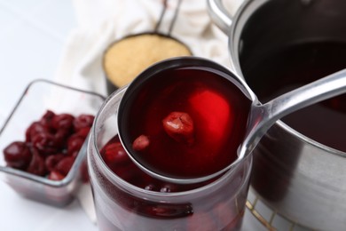 Photo of Pouring tasty cherry compot into glass jar on white table, closeup