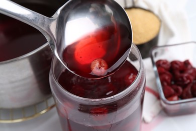 Photo of Pouring tasty cherry compot into glass jar on white table, closeup
