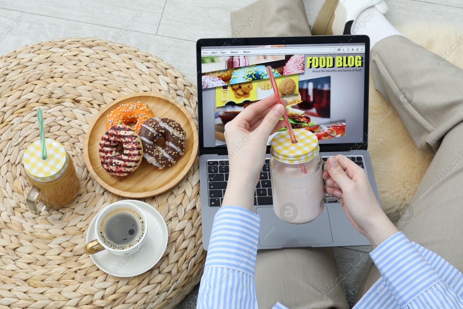 Blogger holding drink near laptop with food blog web site on floor indoors, above view Photo of Blogger holding drink near laptop with food blog web site on floor indoors, above view