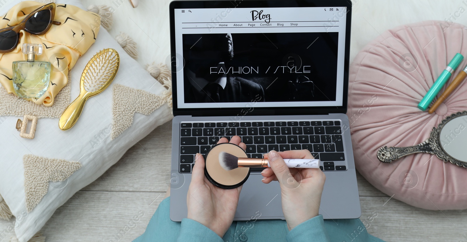 Blogger holding face powder and brush near laptop with fashion blog web site on floor indoors, above view Photo of Blogger holding face powder and brush near laptop with fashion blog web site on floor indoors, above view