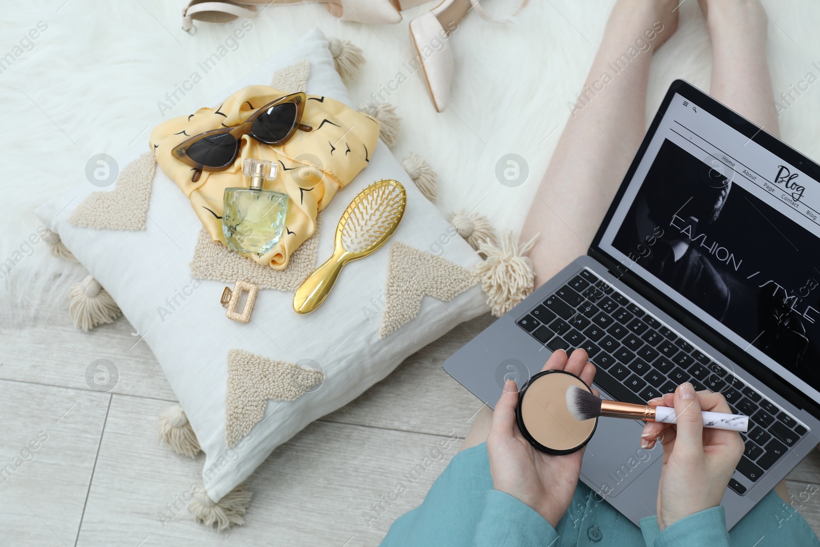 Blogger holding face powder and brush near laptop with fashion blog web site on floor indoors, above view Photo of Blogger holding face powder and brush near laptop with fashion blog web site on floor indoors, above view
