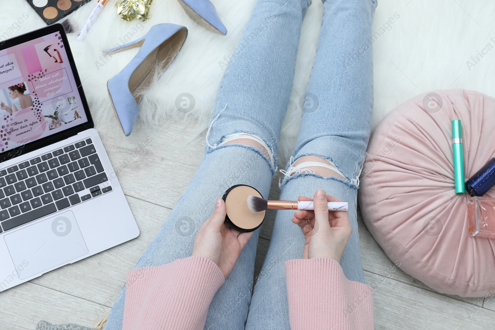 Blogger holding face powder and brush near laptop with beauty blog web site on floor indoors, above view Photo of Blogger holding face powder and brush near laptop with beauty blog web site on floor indoors, above view