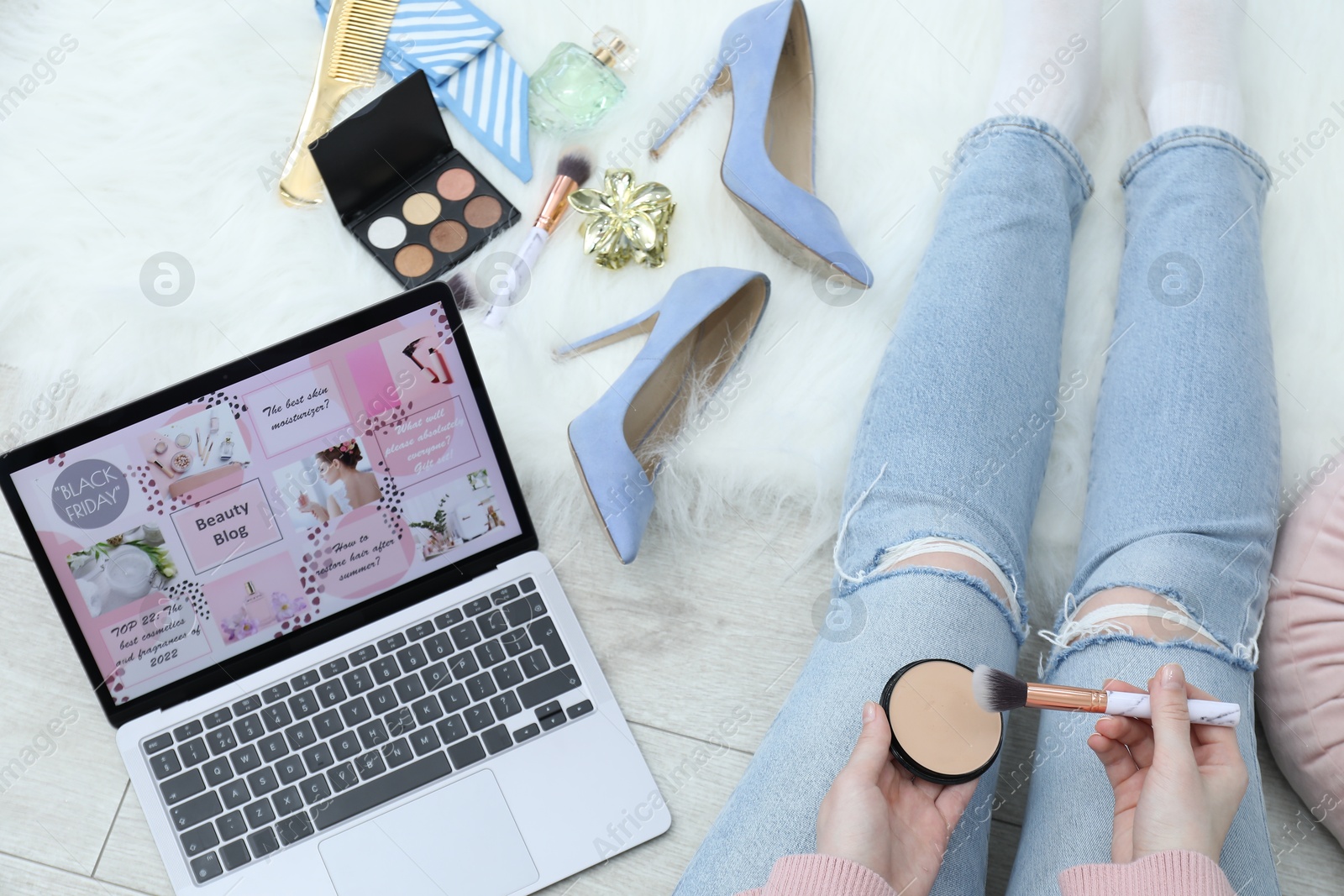 Blogger holding face powder and brush near laptop with beauty blog web site on floor indoors, above view Photo of Blogger holding face powder and brush near laptop with beauty blog web site on floor indoors, above view