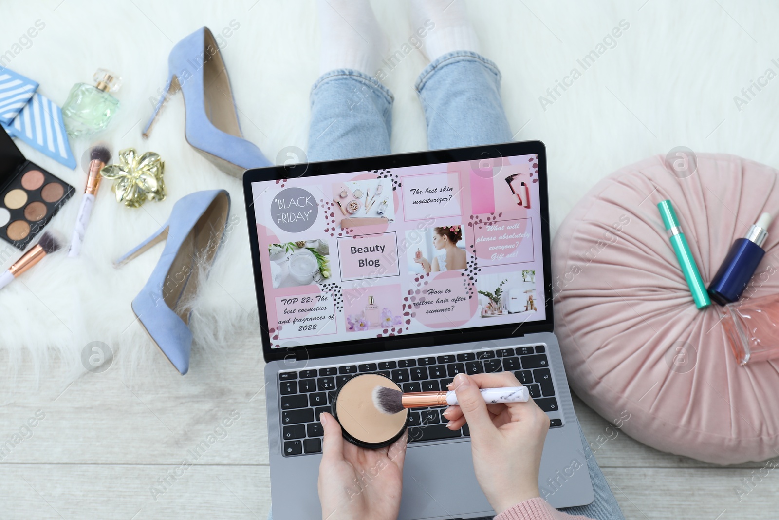 Blogger holding face powder and brush near laptop with beauty blog web site on floor indoors, above view Photo of Blogger holding face powder and brush near laptop with beauty blog web site on floor indoors, above view