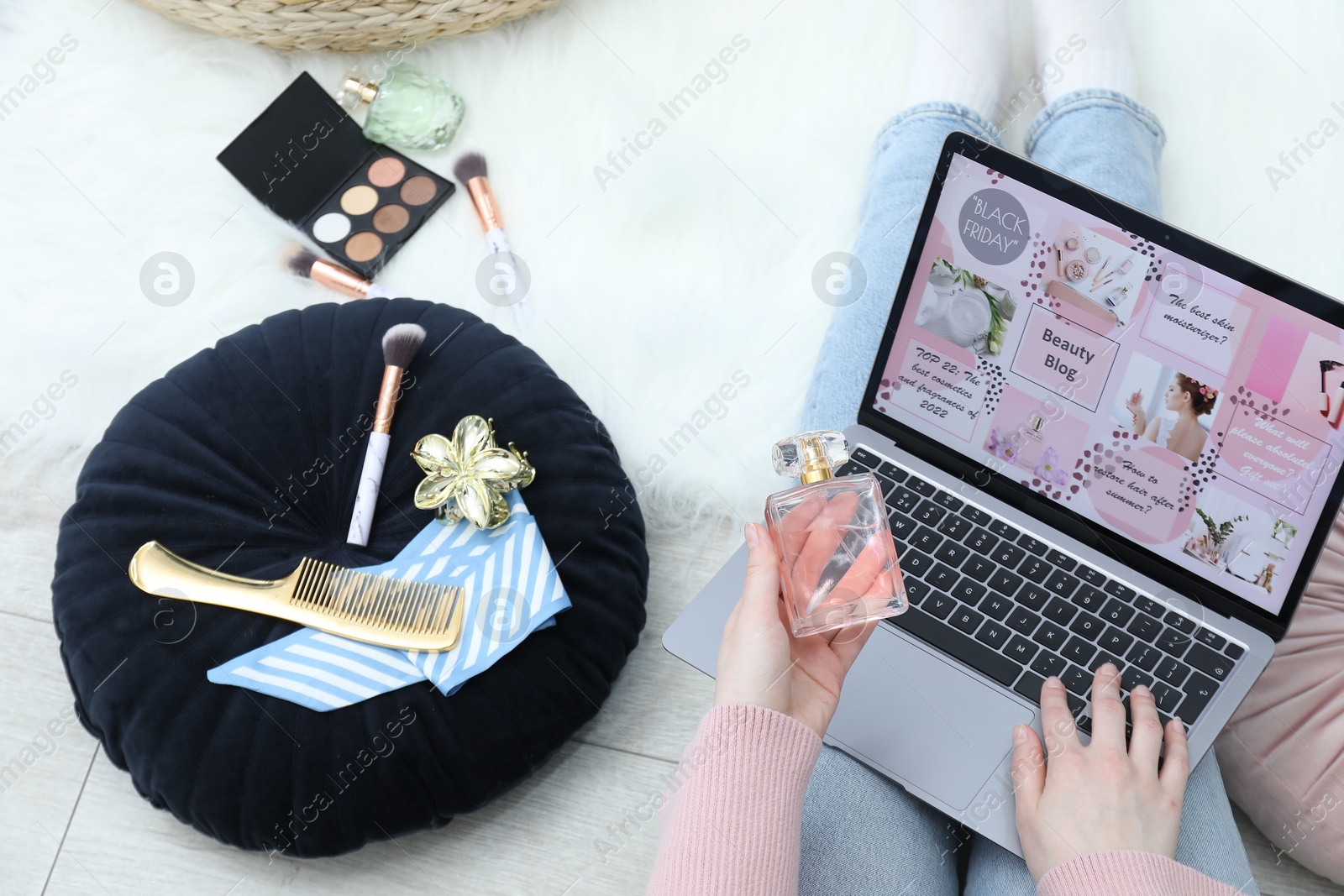 Blogger holding perfume near laptop with beauty blog web site on floor indoors, above view Photo of Blogger holding perfume near laptop with beauty blog web site on floor indoors, above view