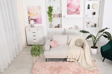 Photo of Comfortable sofa with blanket and green houseplants in living room