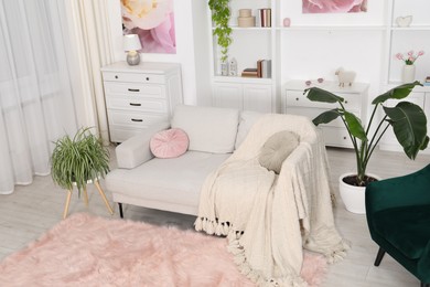 Photo of Comfortable sofa with blanket and green houseplants in living room