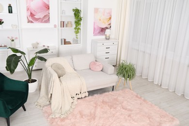 Photo of Comfortable sofa with blanket and green houseplants in living room