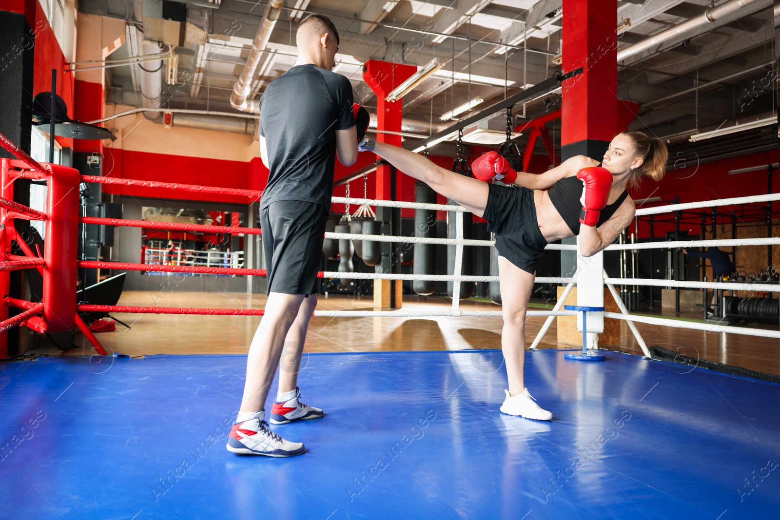 Woman in protective gloves having boxing practice with her coach at training center, low angle view Photo of Woman in protective gloves having boxing practice with her coach at training center, low angle view