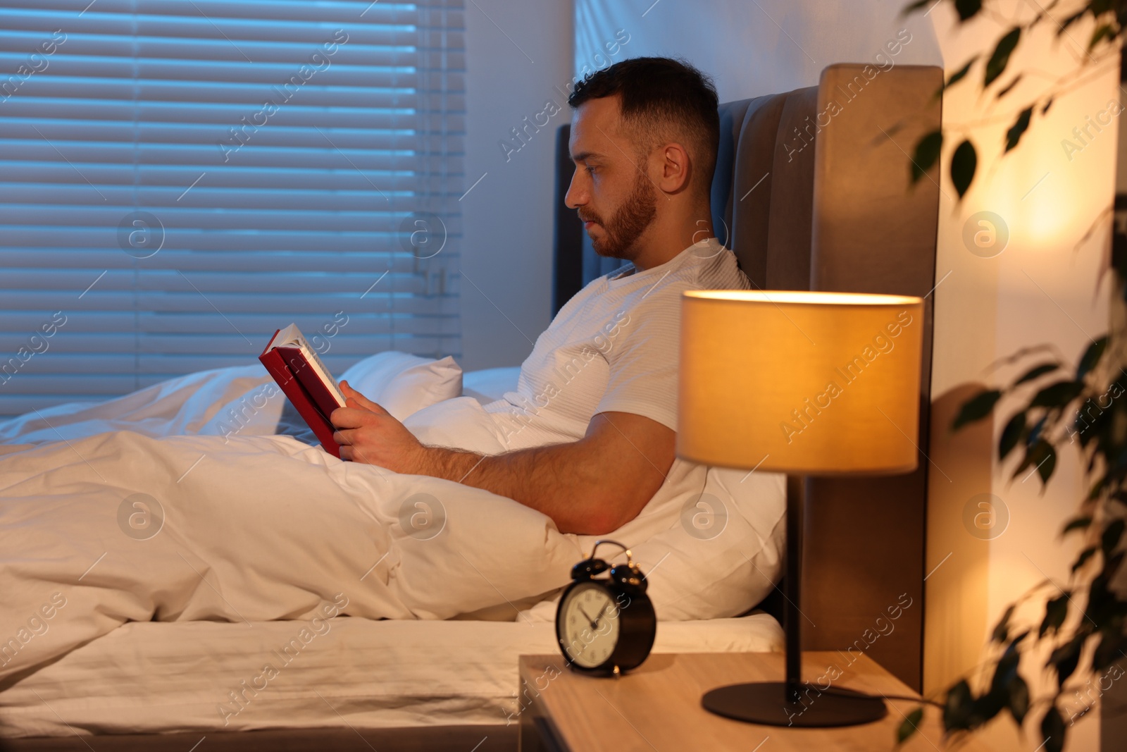 Young man reading book in bed at home Photo of Young man reading book in bed at home