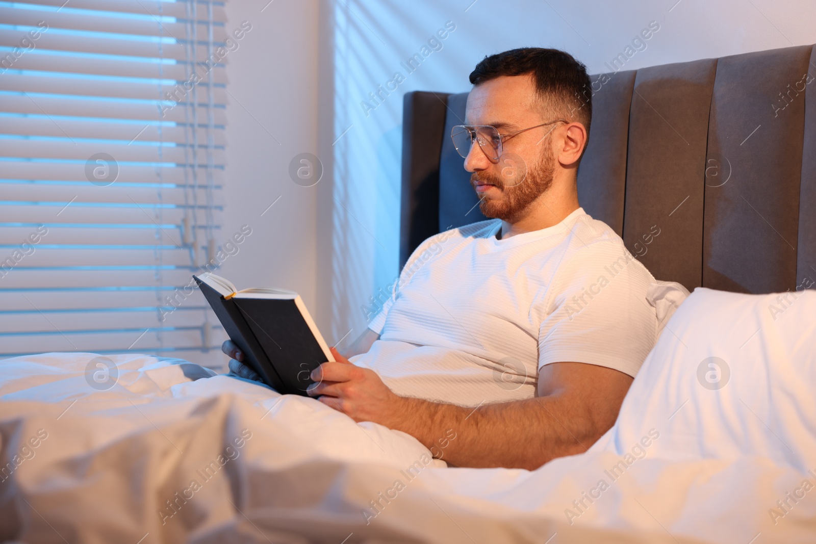 Young man reading book in bed at home Photo of Young man reading book in bed at home