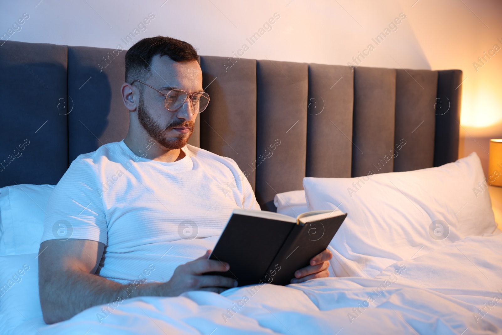 Young man reading book in bed at home Photo of Young man reading book in bed at home