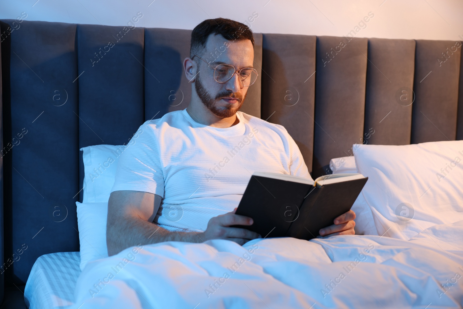 Young man reading book in bed at home Photo of Young man reading book in bed at home