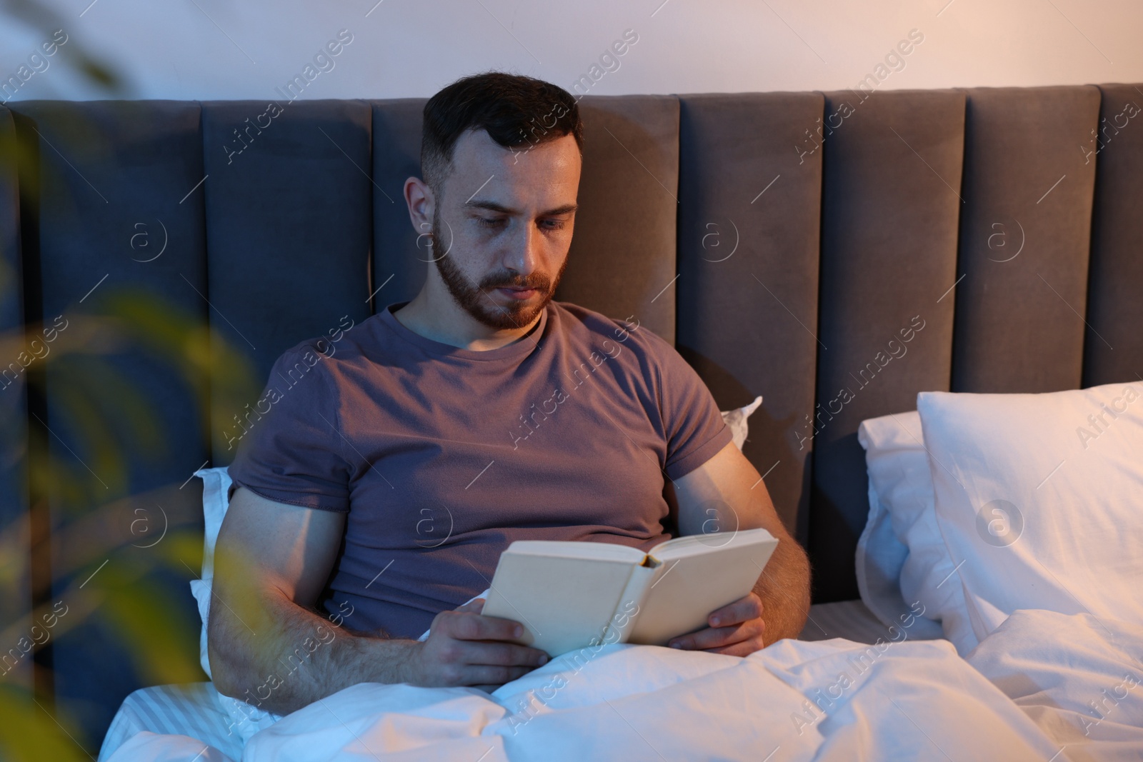 Young man reading book in bed at home Photo of Young man reading book in bed at home