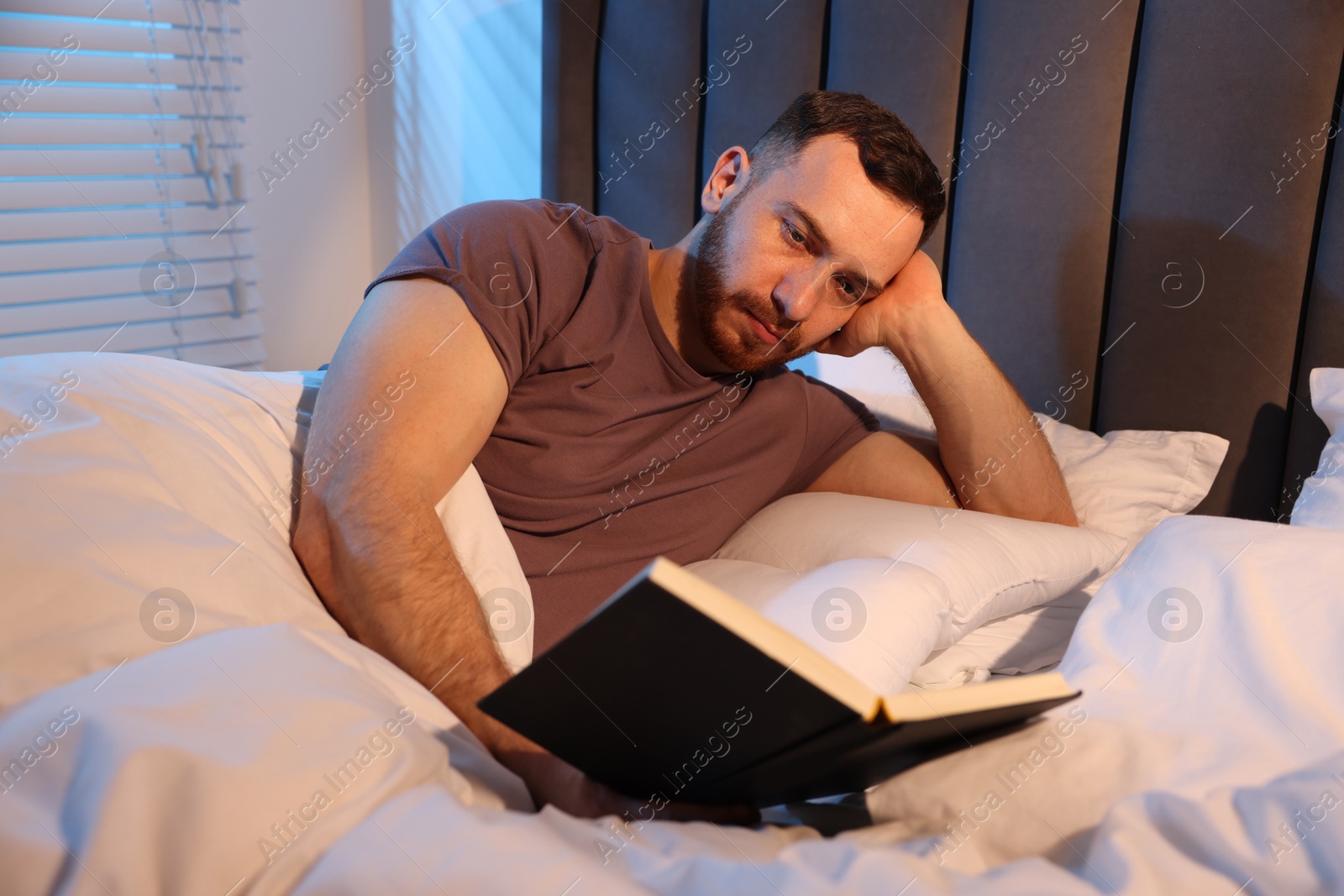 Young man reading book in bed at home Photo of Young man reading book in bed at home