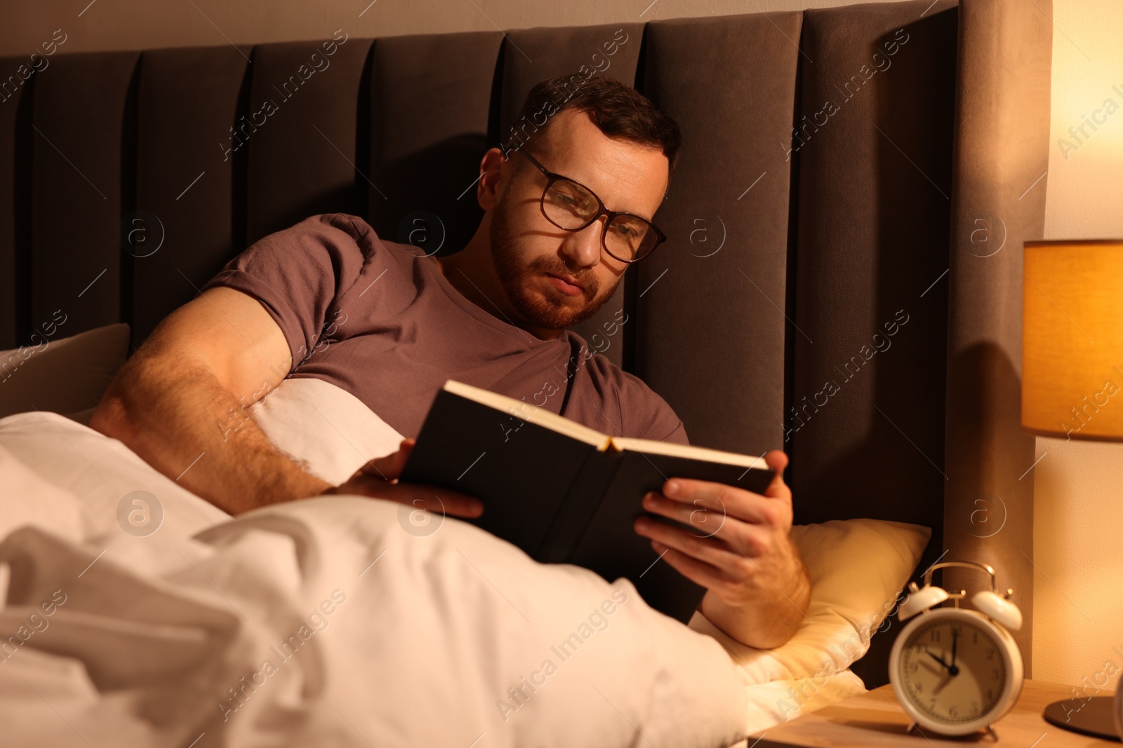 Young man reading book in bed at home Photo of Young man reading book in bed at home