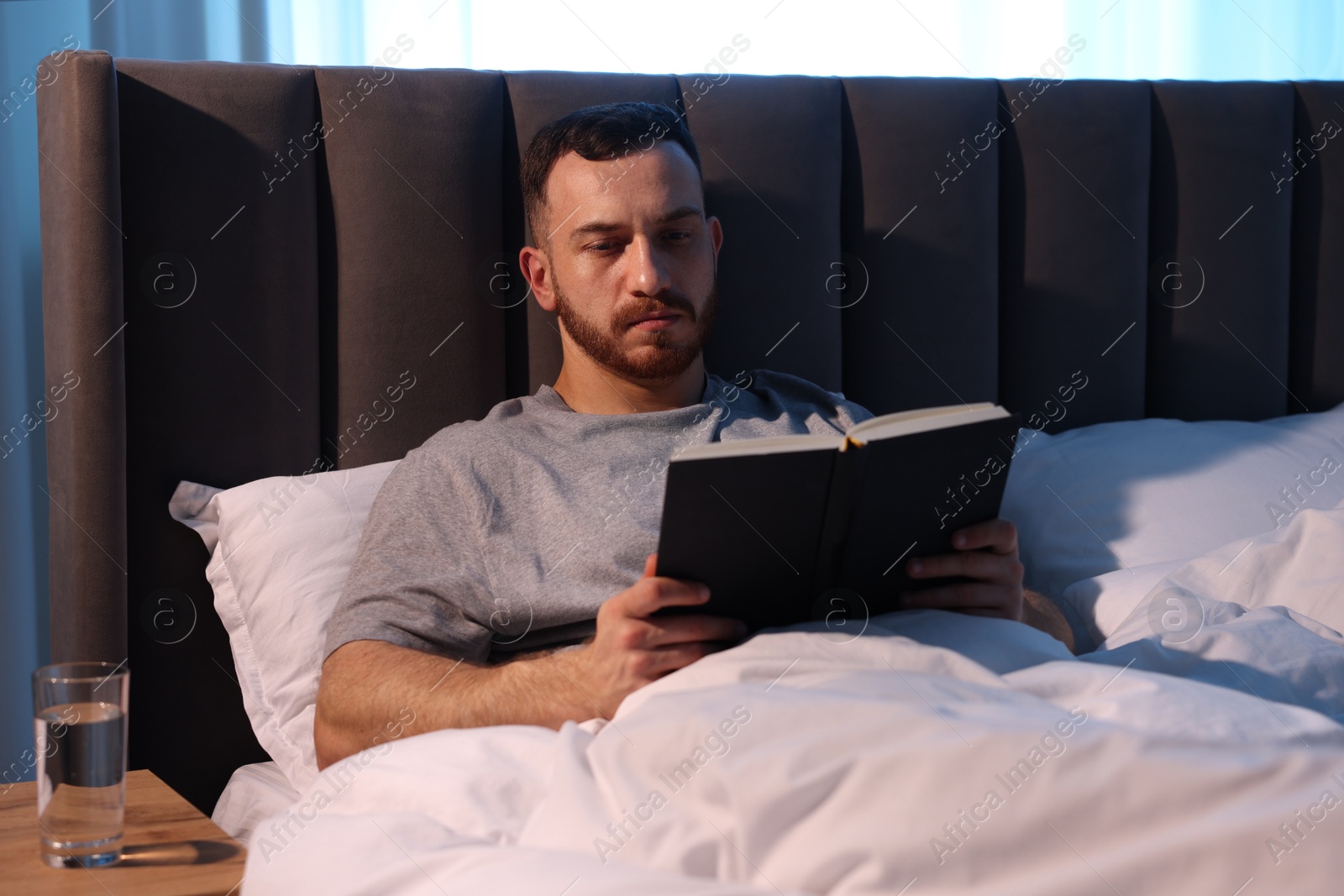 Young man reading book in bed at home Photo of Young man reading book in bed at home