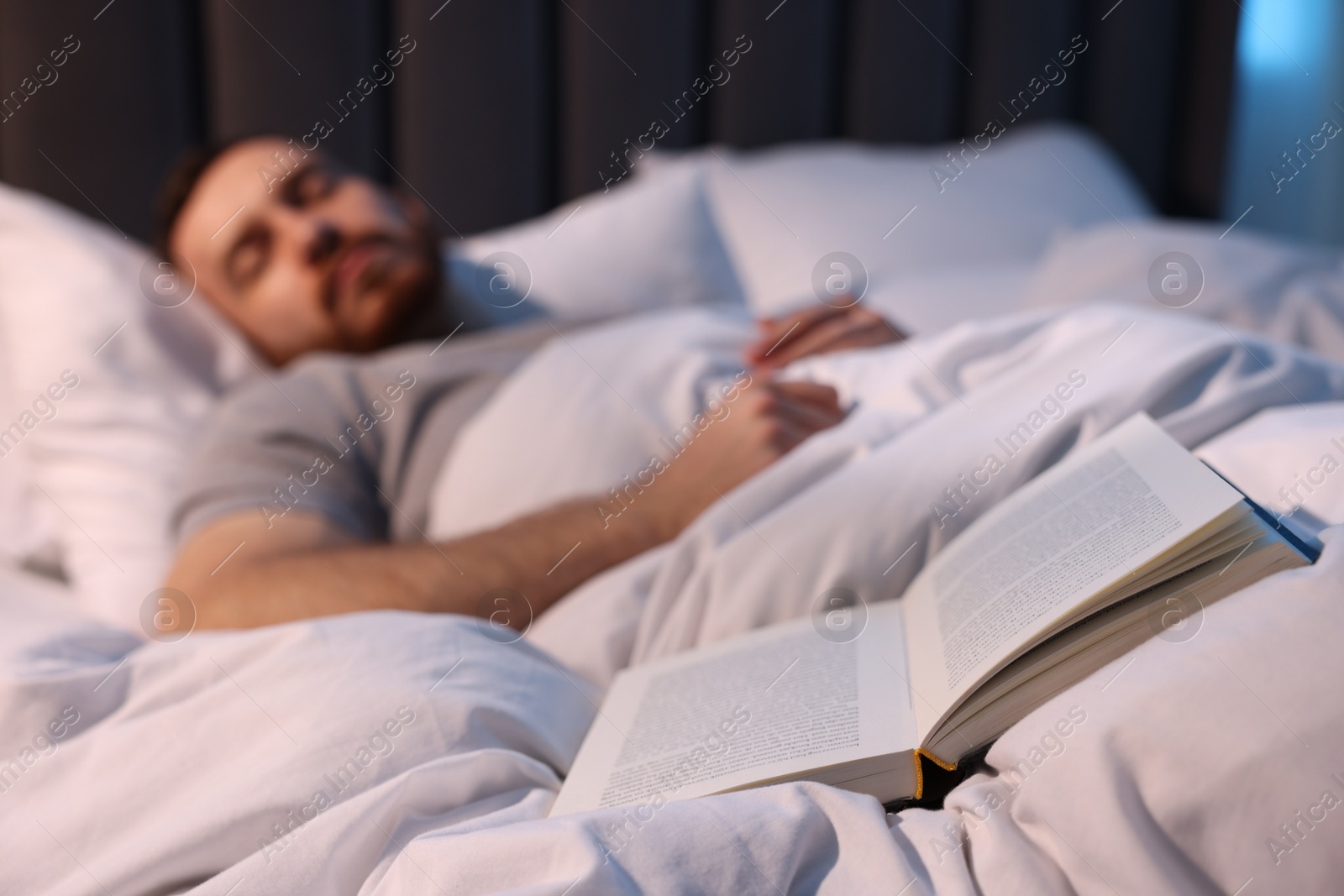 Young man sleeping in bed at home, focus on book Photo of Young man sleeping in bed at home, focus on book