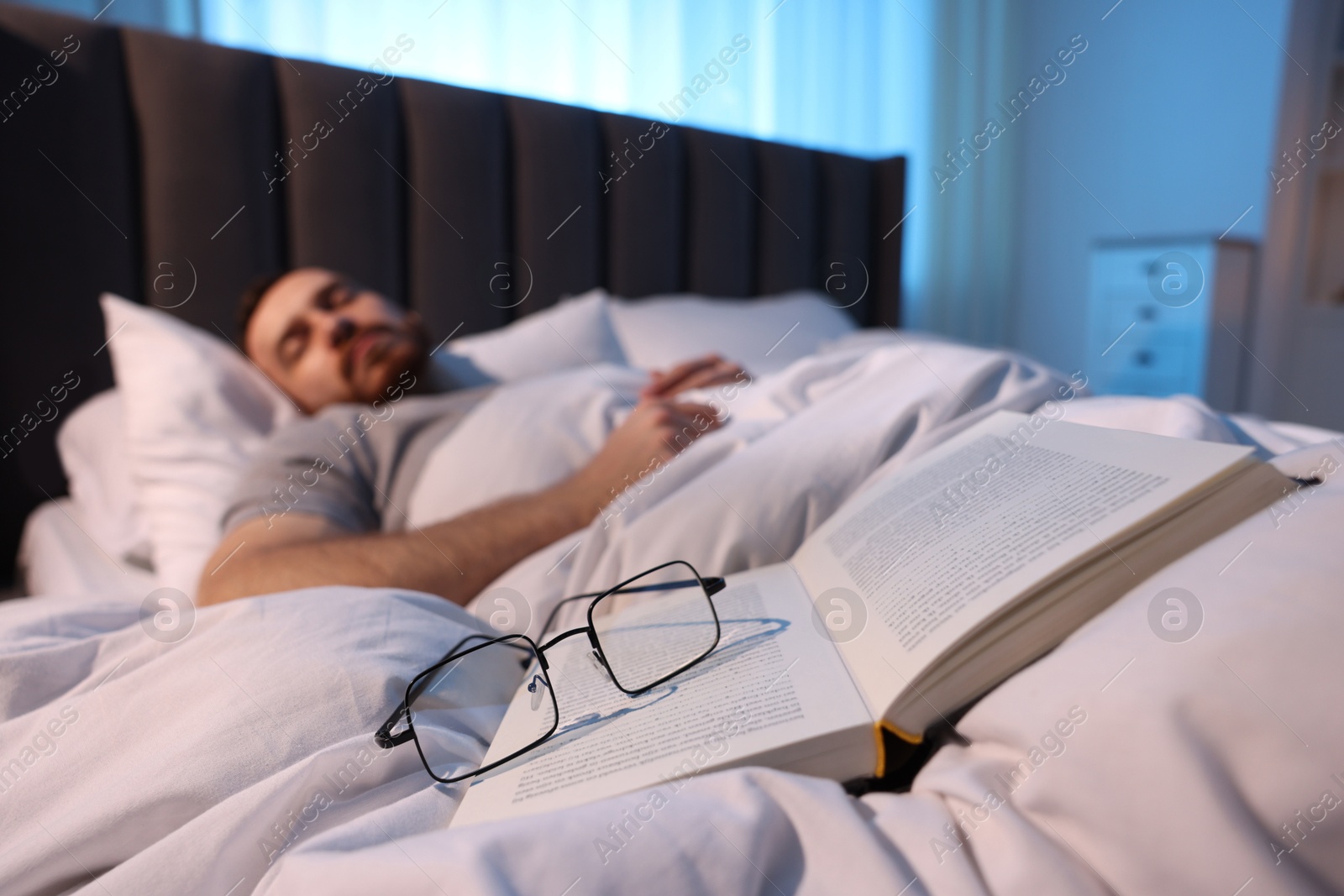 Young man sleeping in bed at home, focus on book and glasses Photo of Young man sleeping in bed at home, focus on book and glasses