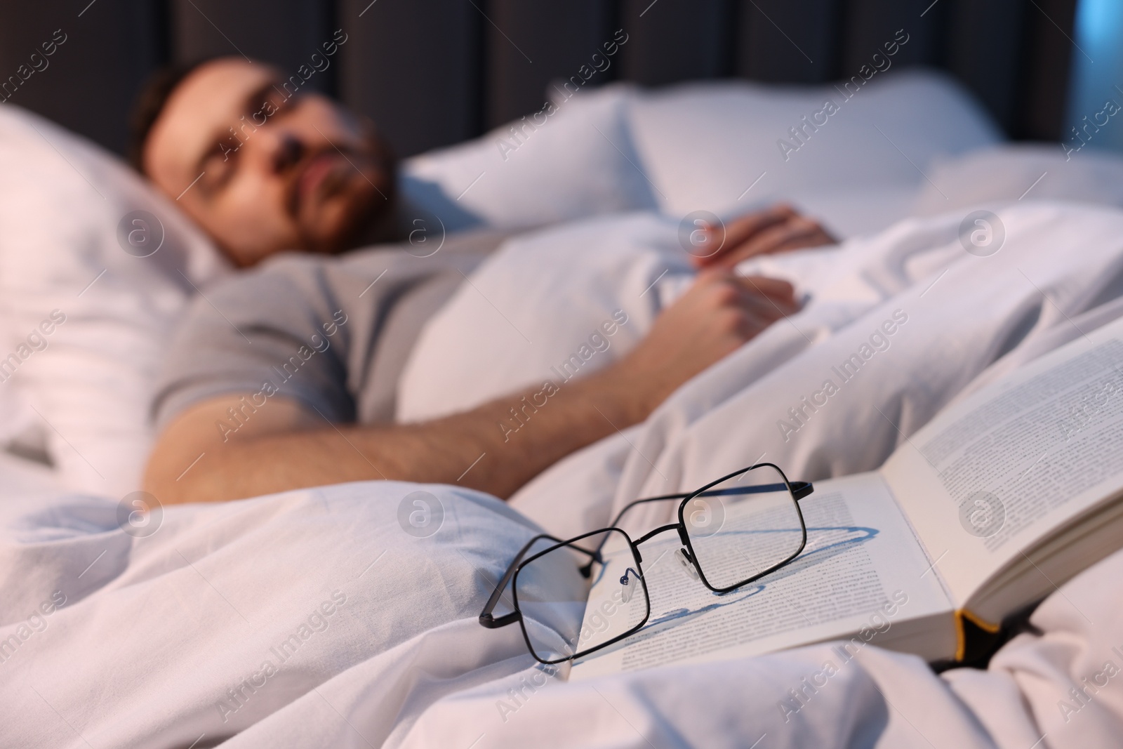 Young man sleeping in bed at home, focus on book and glasses Photo of Young man sleeping in bed at home, focus on book and glasses