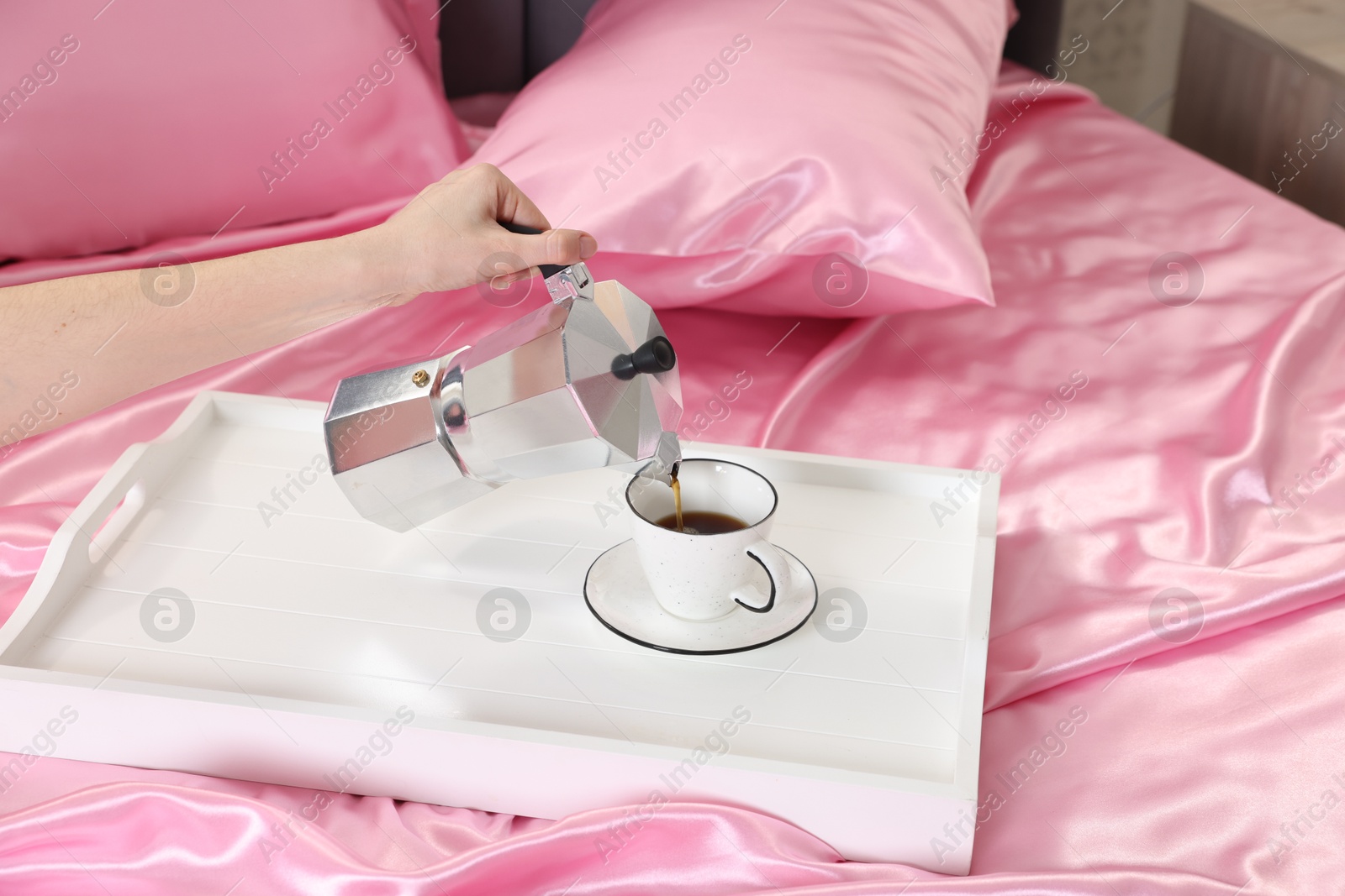 Woman pouring coffee from moka pot into cup on bed with silk linens, closeup Photo of Woman pouring coffee from moka pot into cup on bed with silk linens, closeup