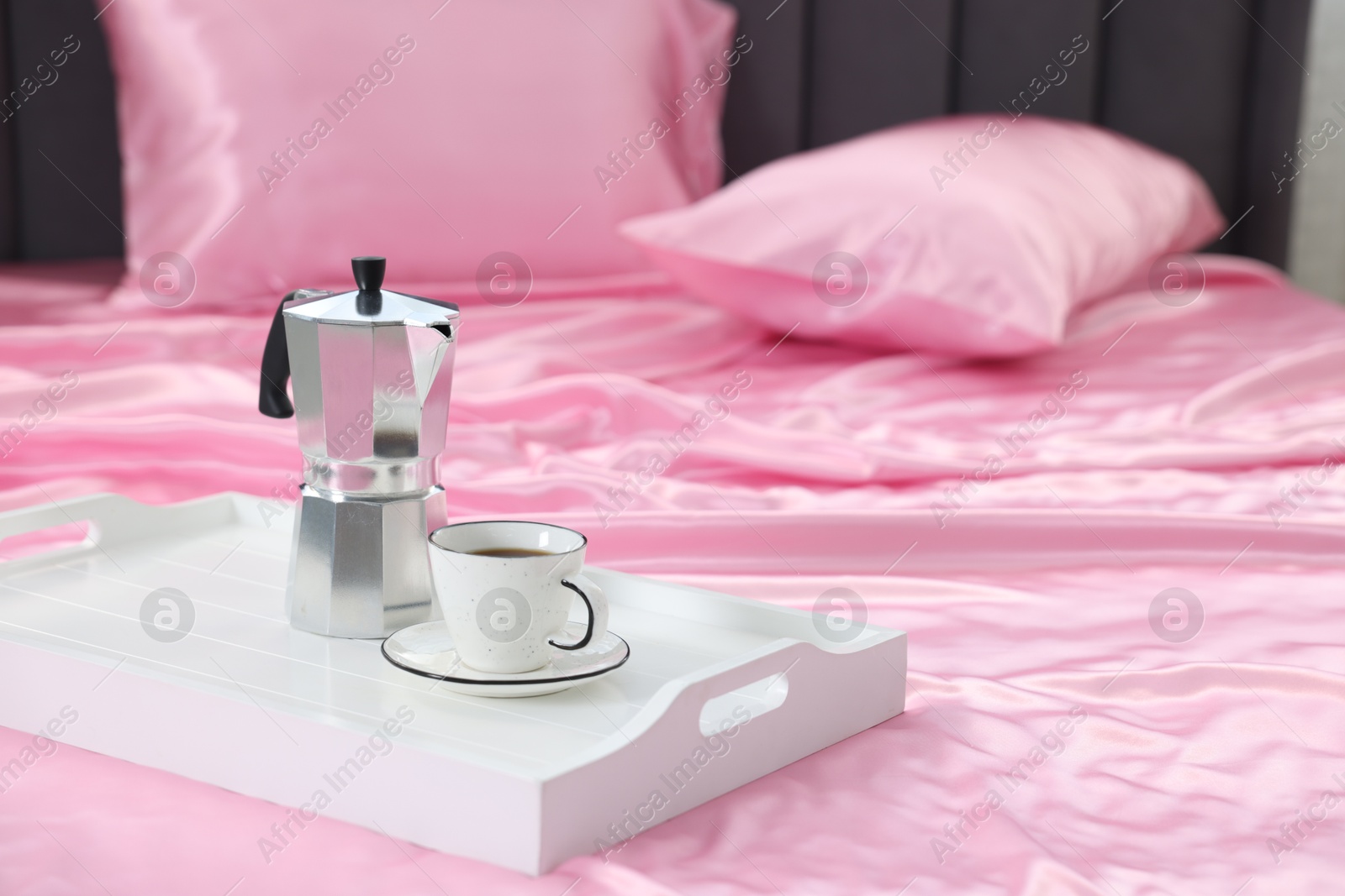Moka pot and cup of coffee on bed with silk linens, closeup Photo of Moka pot and cup of coffee on bed with silk linens, closeup